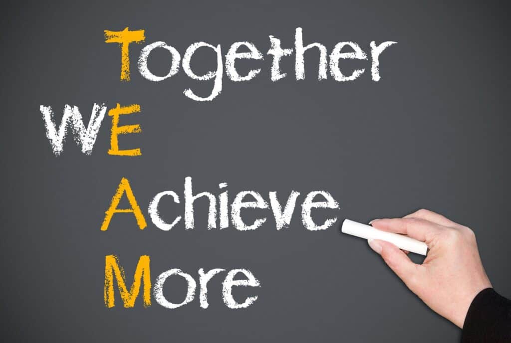  A supervisor is seen writing on a blackboard with the words 'Together We Achieve More' to illustrate the concept of a supervisor leading and motivating a team.